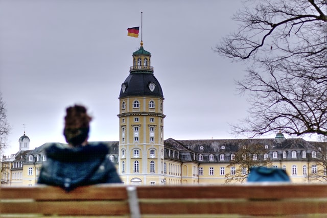 Mann sitzt auf Bank vor dem Schloss Karlsruhe
